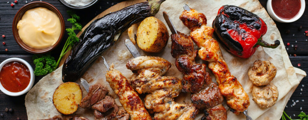 Various grilled meat including chicken and beef kebabs, potatoes, a red pepper and aubergine.