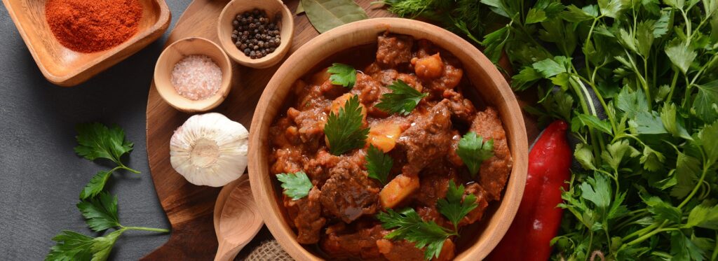 Pot of goulash surrounded by herbs and spices