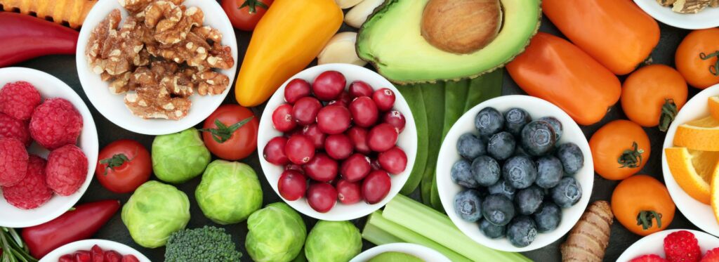 Fresh fruit and vegetables in bowls and on a table, along with some nuts.