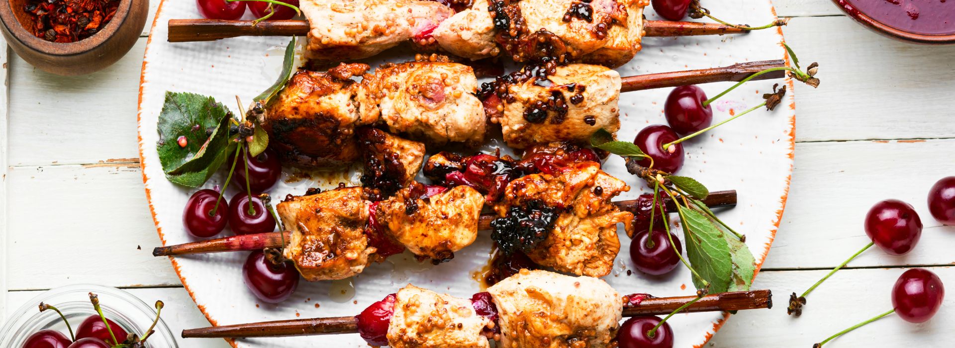 Marinated chicken sosaties on white plate with cherries